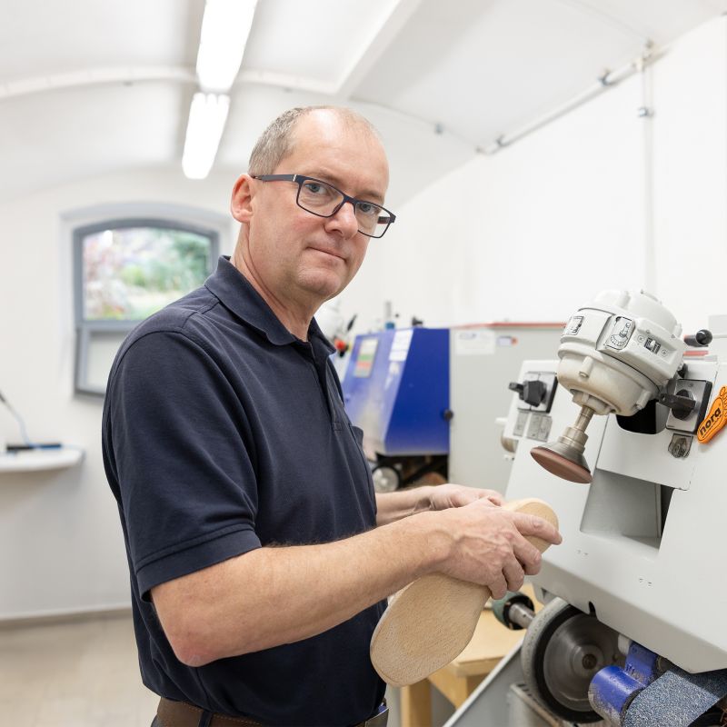 Portrait eines Mannes im dunkelblauen T-Shirt vor einer Schleifmaschine
