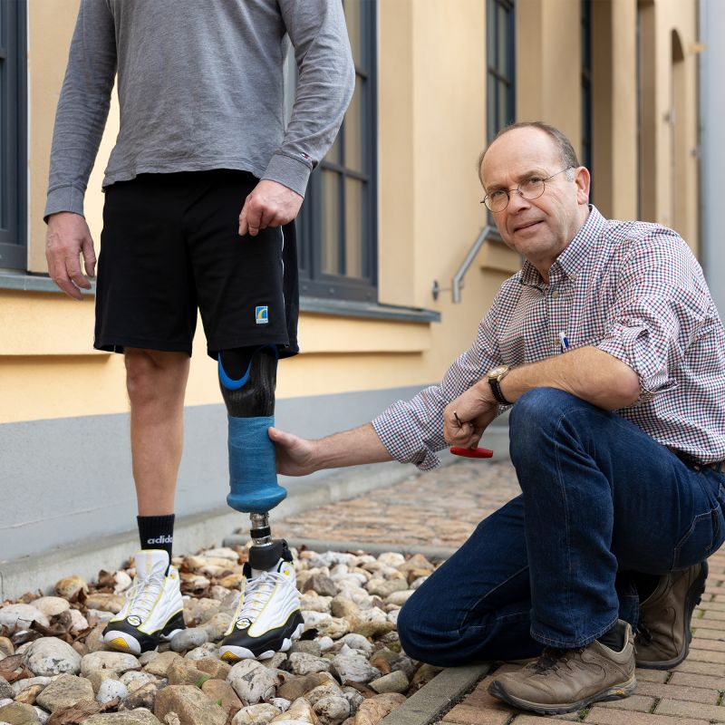 Mann kniet neben einem Prothesenträger und passt die Prothese an