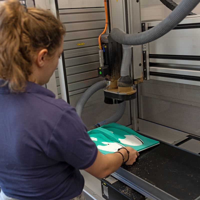 Mitarbeiterin im dunkelblauem Shirt nimmt eine gefräßte Einlage aus der Maschine