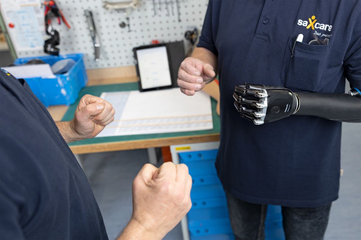 zwei Personen stehen sich gegenüber, die Person mit der Armprothese spiegelt die Handbewegungen