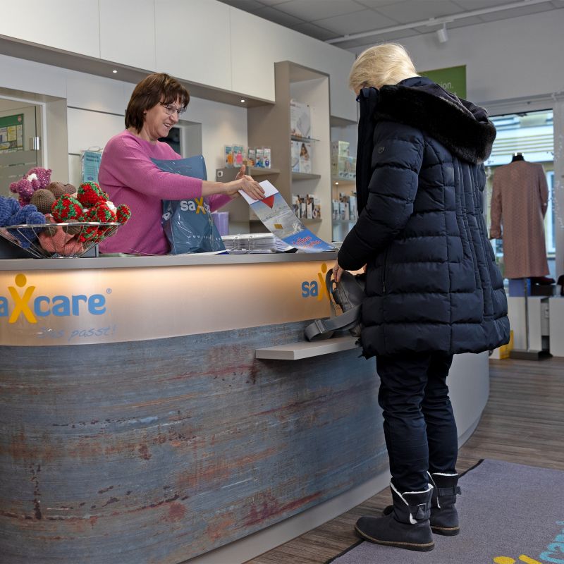 Mitarbeiterin übergibt Kundin einen Kalender und gekaufte Produkte