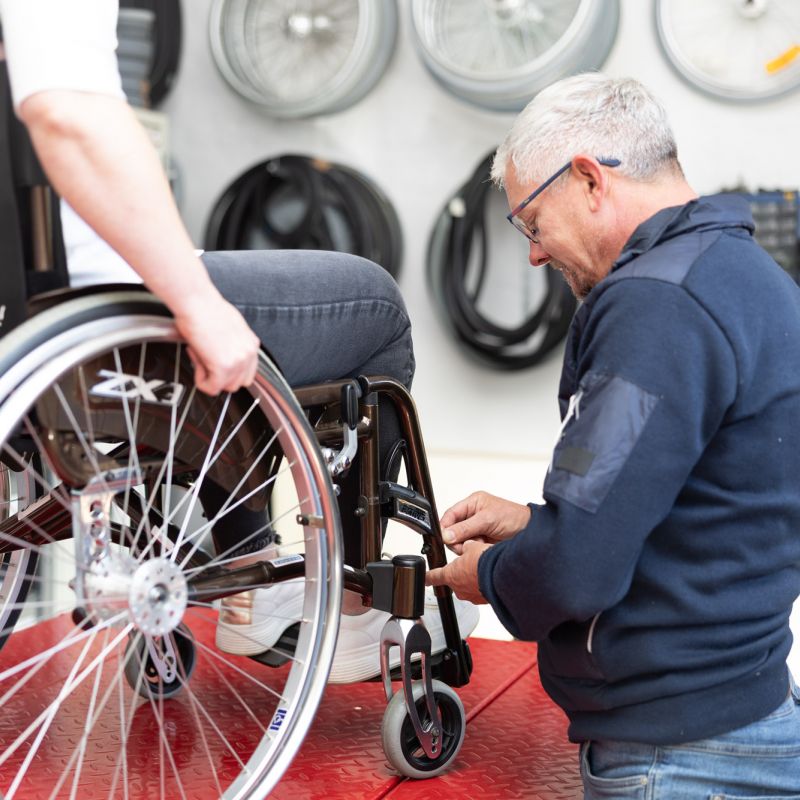 saXcare Mitarbeiter schraubt an einem Rollstuhl um die Höhe der Füßstützen anzupassen