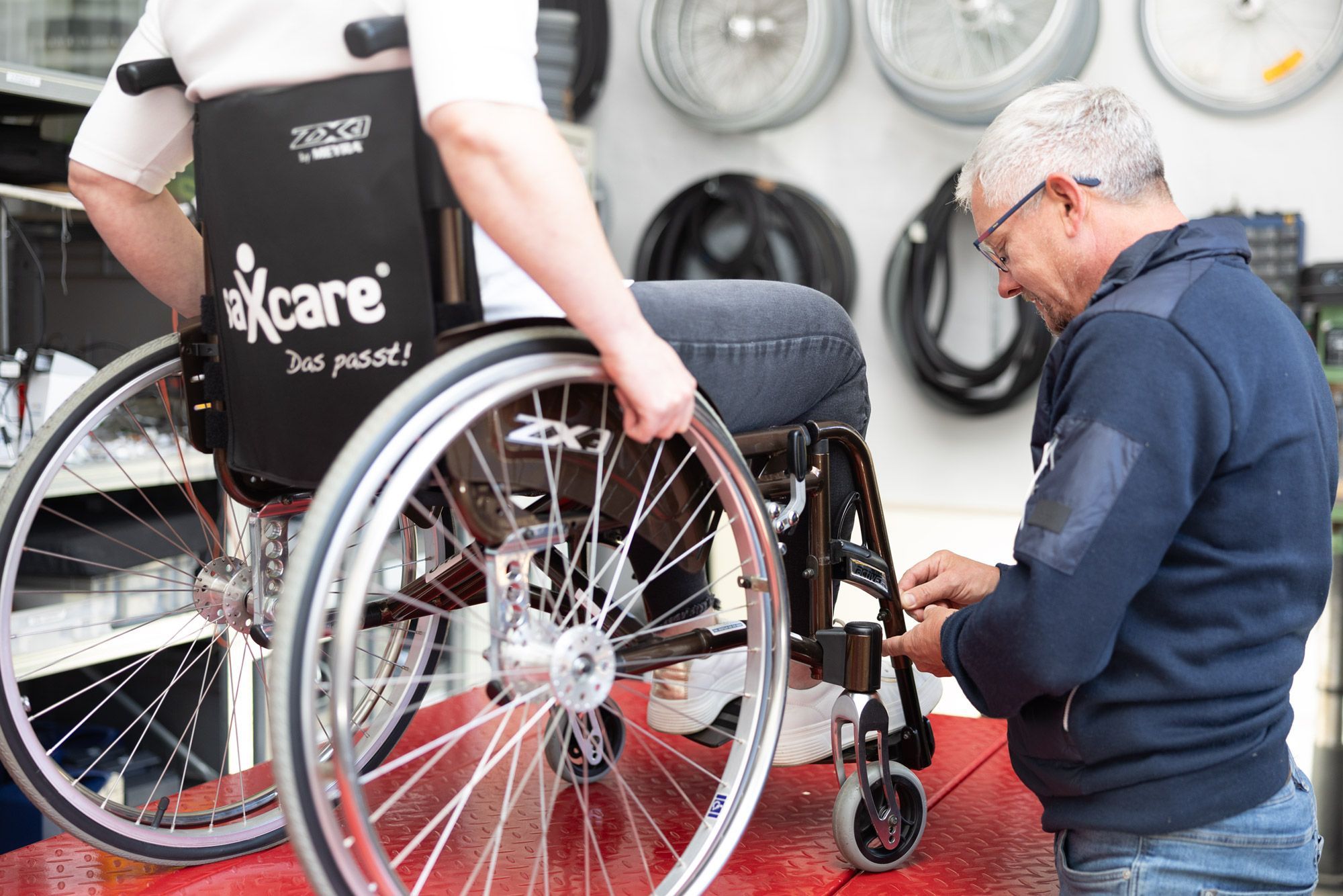 saXcare Mitarbeiter schraubt an einem Rollstuhl um die Höhe der Füßstützen anzupassen
